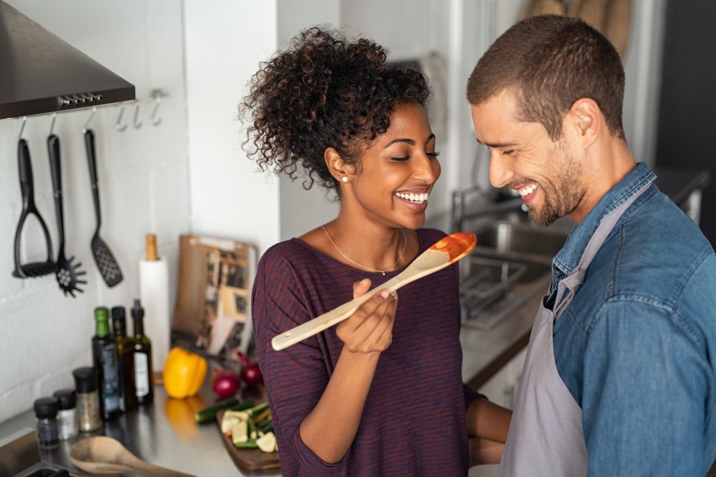 Young,Couple,Tasting,Tomato,Sauce,While,Cooking,In,The,Kitchen.